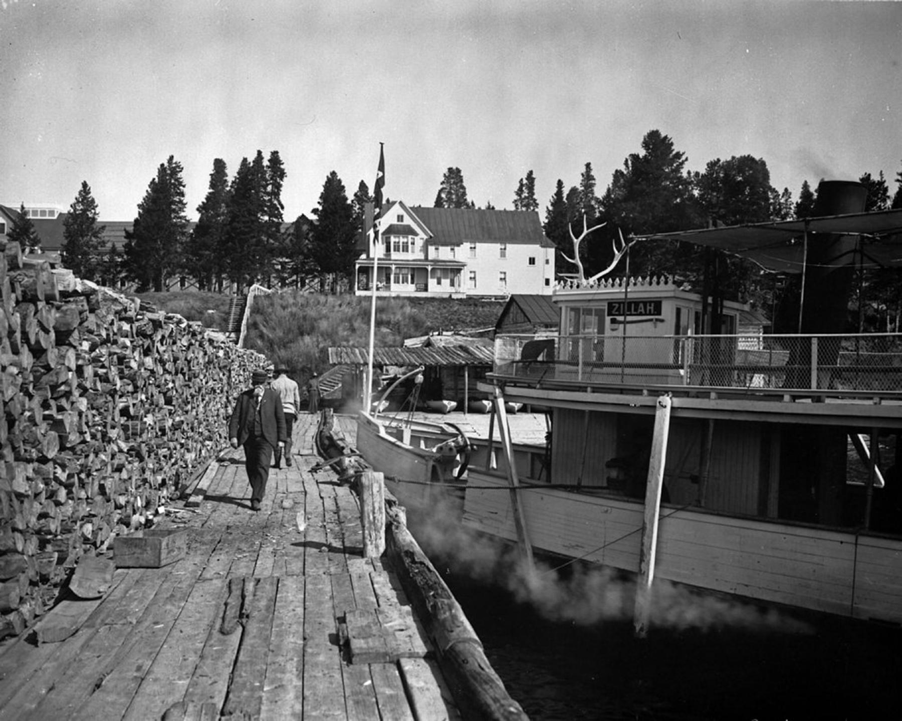 The steamer Zillah docked at the Lake Hotel with small rental boats under a shed behind it, 1904
